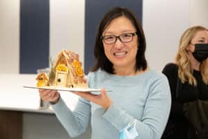 Asian woman with glasses holding charcuterie chalet with salami shingles and swiss cheese snowmanJPG
