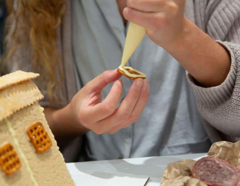 hands piping cheese onto pretzel while building charcuterie chalet