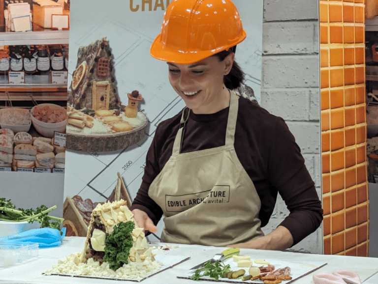 Woman in hard hat looking at A-frame edible architecture house covered in cheese