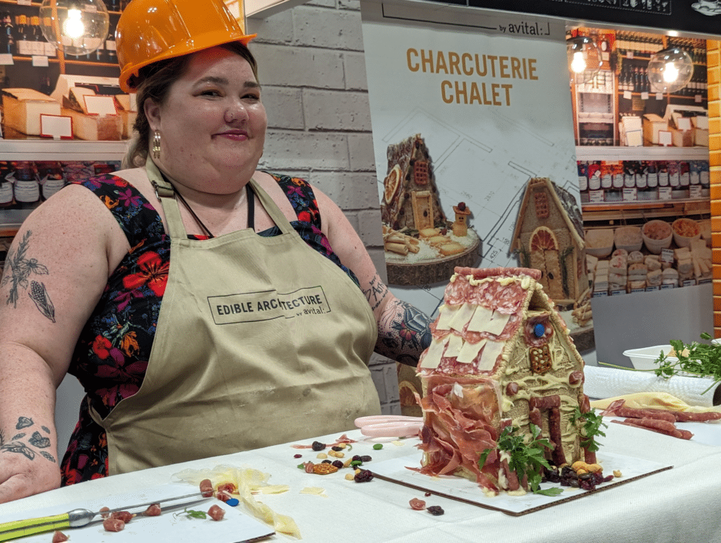 contestant wearing hard hat and apron smiling at camera with charcuterie Chalet decorated