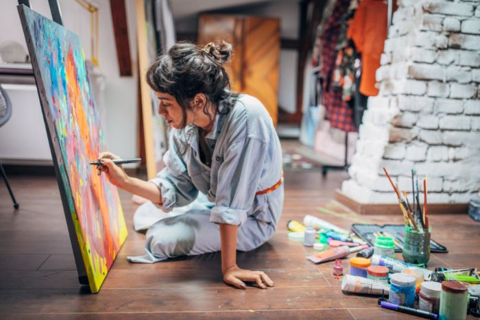 artist sitting on floor painting on canvas