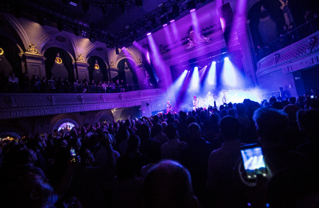 A band is on stage while a large crowd dances and lights flash at August Hall SF