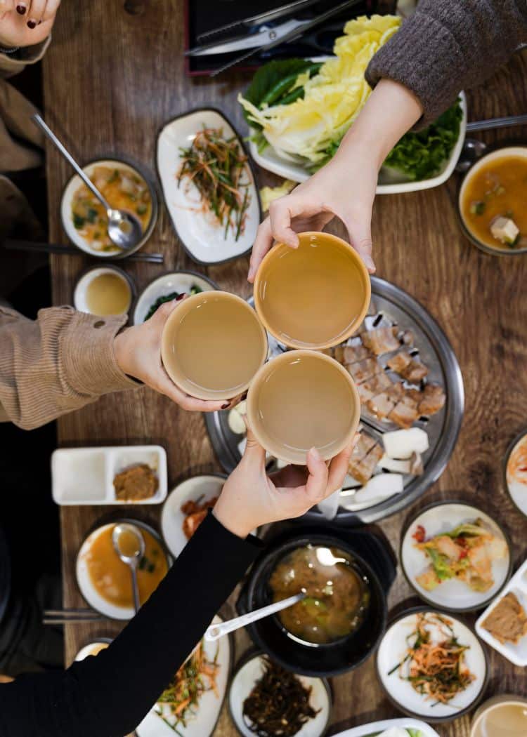 hands toasting drinks over table of korean bbq during koreatown food tour in los angeles