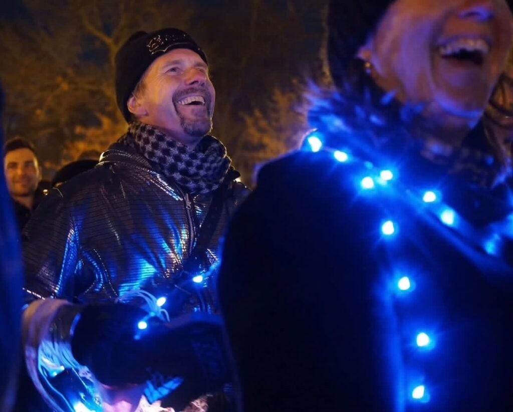 two men wearing christmas lights around their necks smile