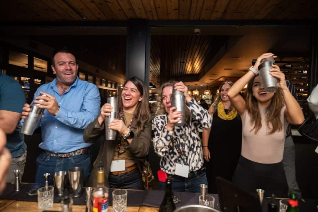 A lively group of people shaking cocktails during a private dining event, showcasing a fun and interactive alternative to a private dining room NYC offers. This dynamic moment highlights how hands-on experiences can add excitement to your gathering.