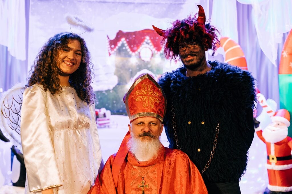 an angel a priest and a devil pose at a holiday party