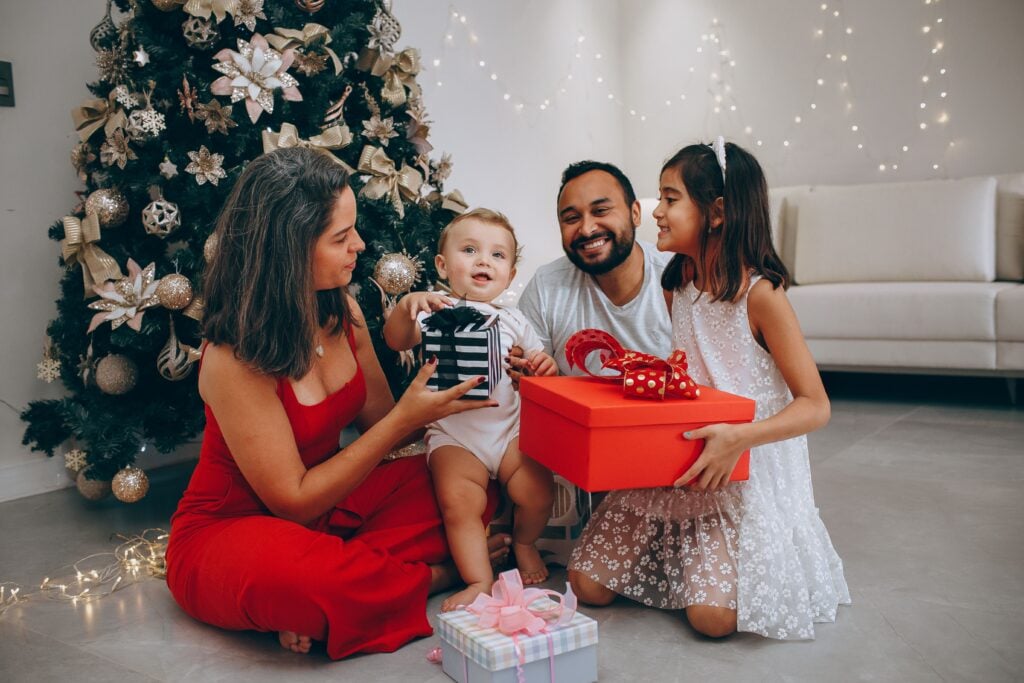 a family smiles under the christmas tree as they open presents