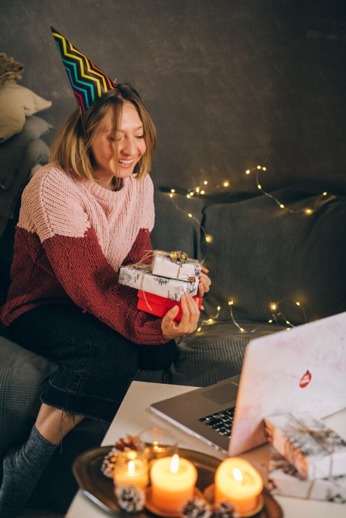 a woman holds wrapped gifts up to her computer screen