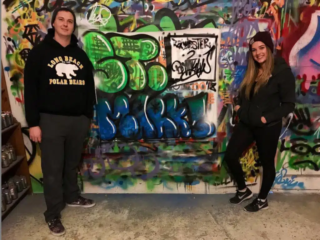 Two friends pose in front of a graffiti wall on a graffiti tour of Brooklyn