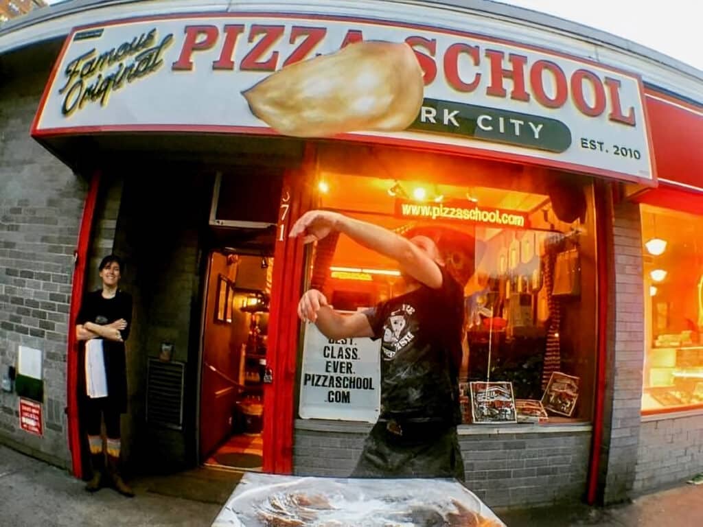 A man flips a pizza outside of Pizza School NYc