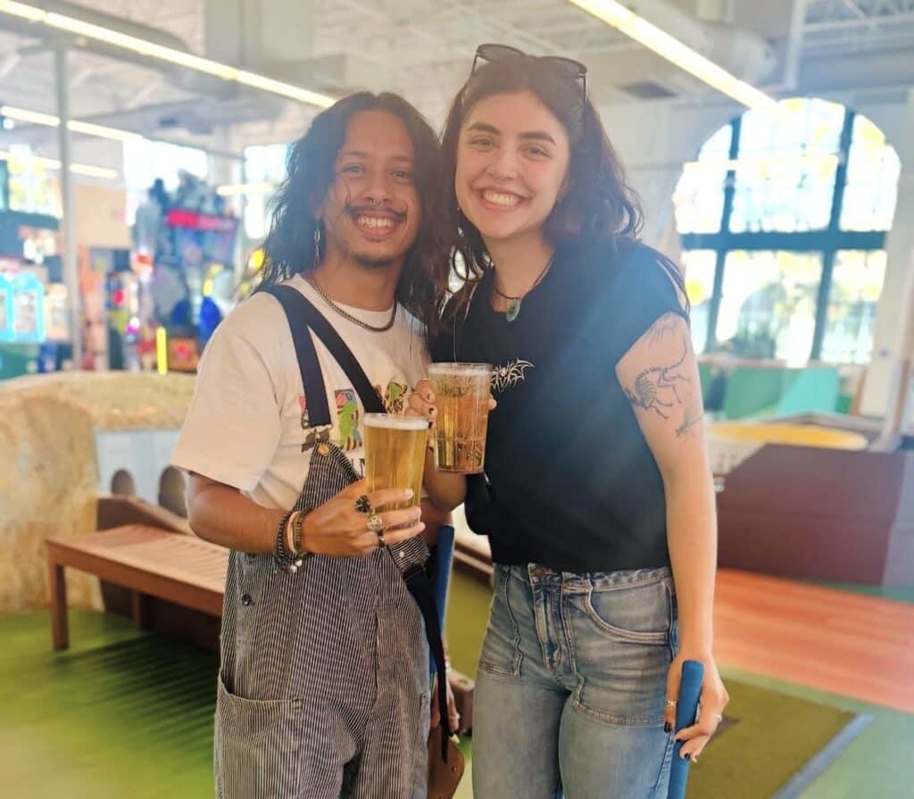 Two people pose with beers while playing mini golf at Subpar