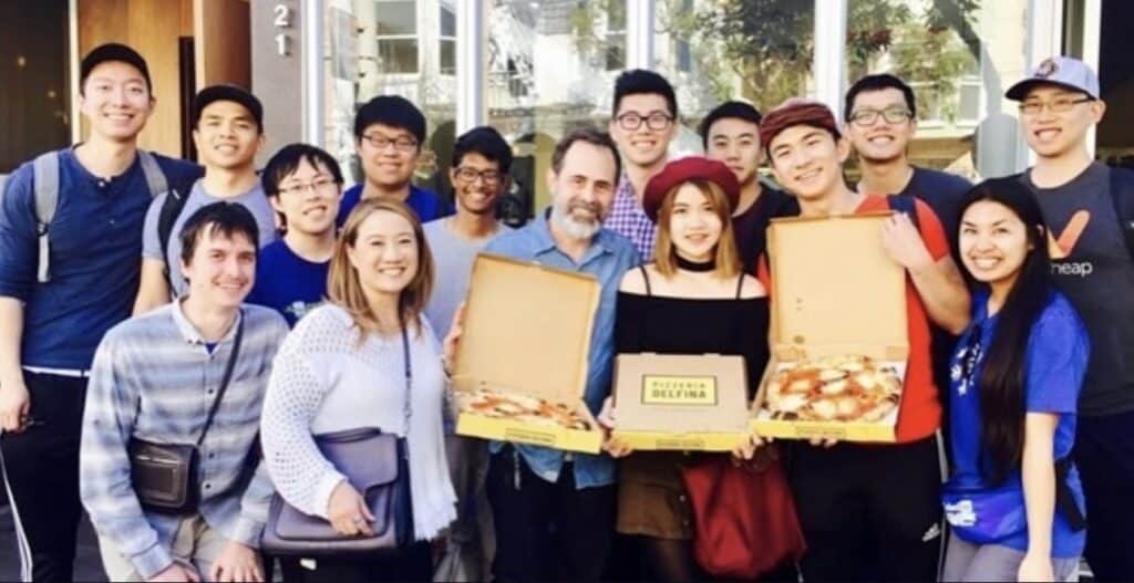 A tour group poses with open pizza boxes on a Sidewalk Food Tour in Sf
