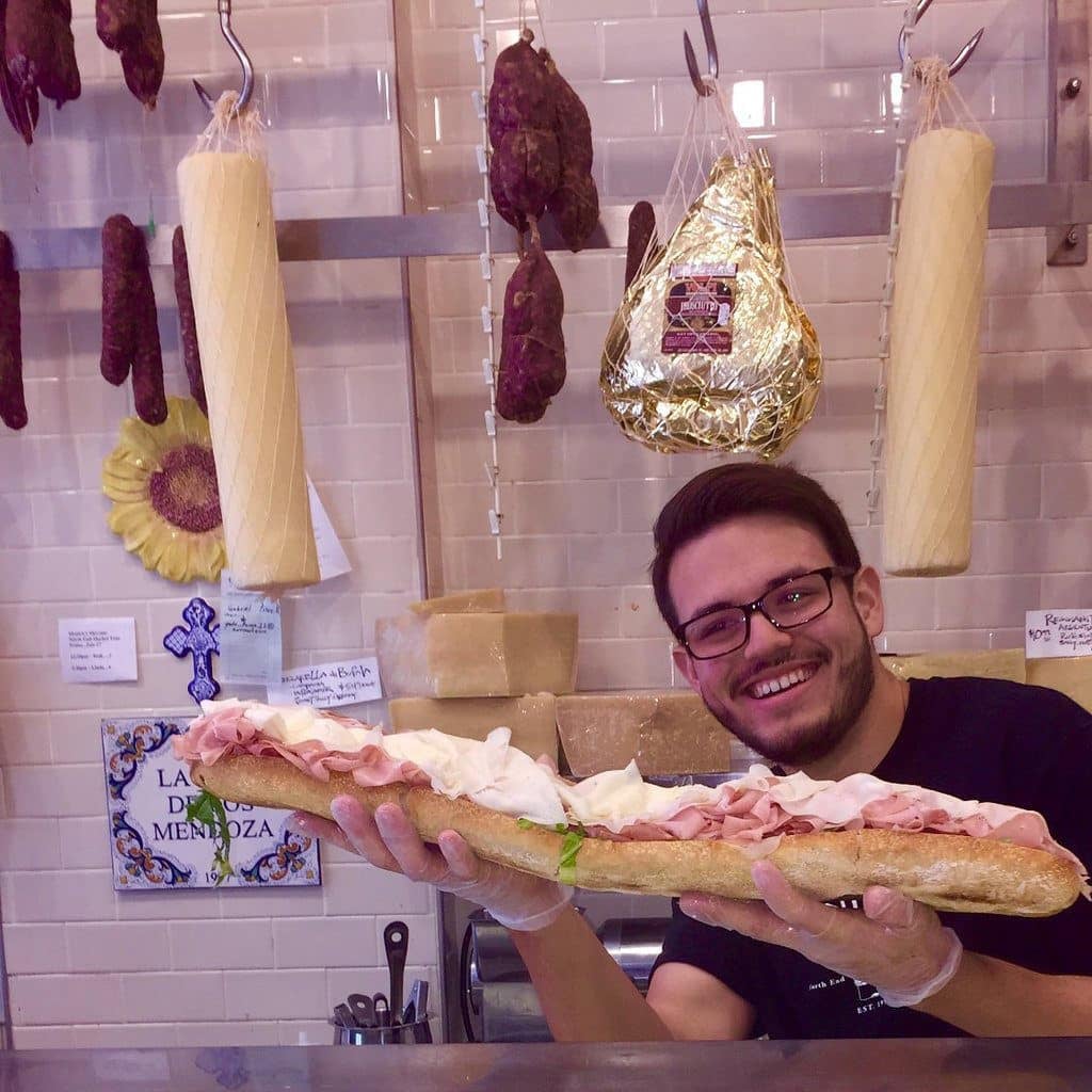 A huge sub sandwhich piled high with cold cuts is shown off by a happy customer