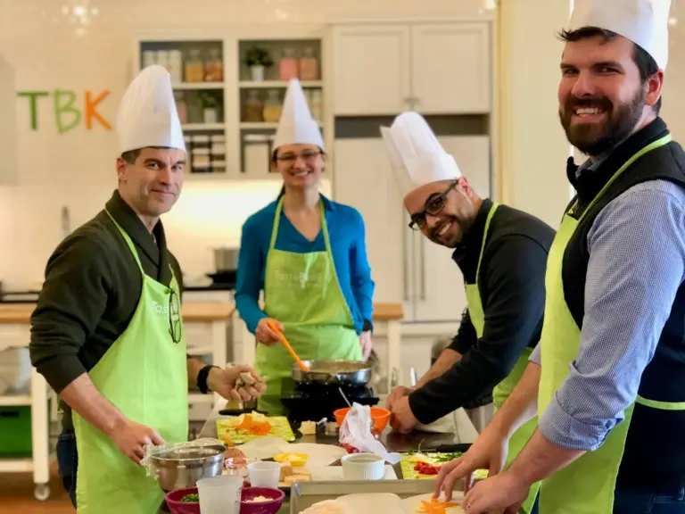 Friends smile at a Taste Buds Kitchen team building cooking class