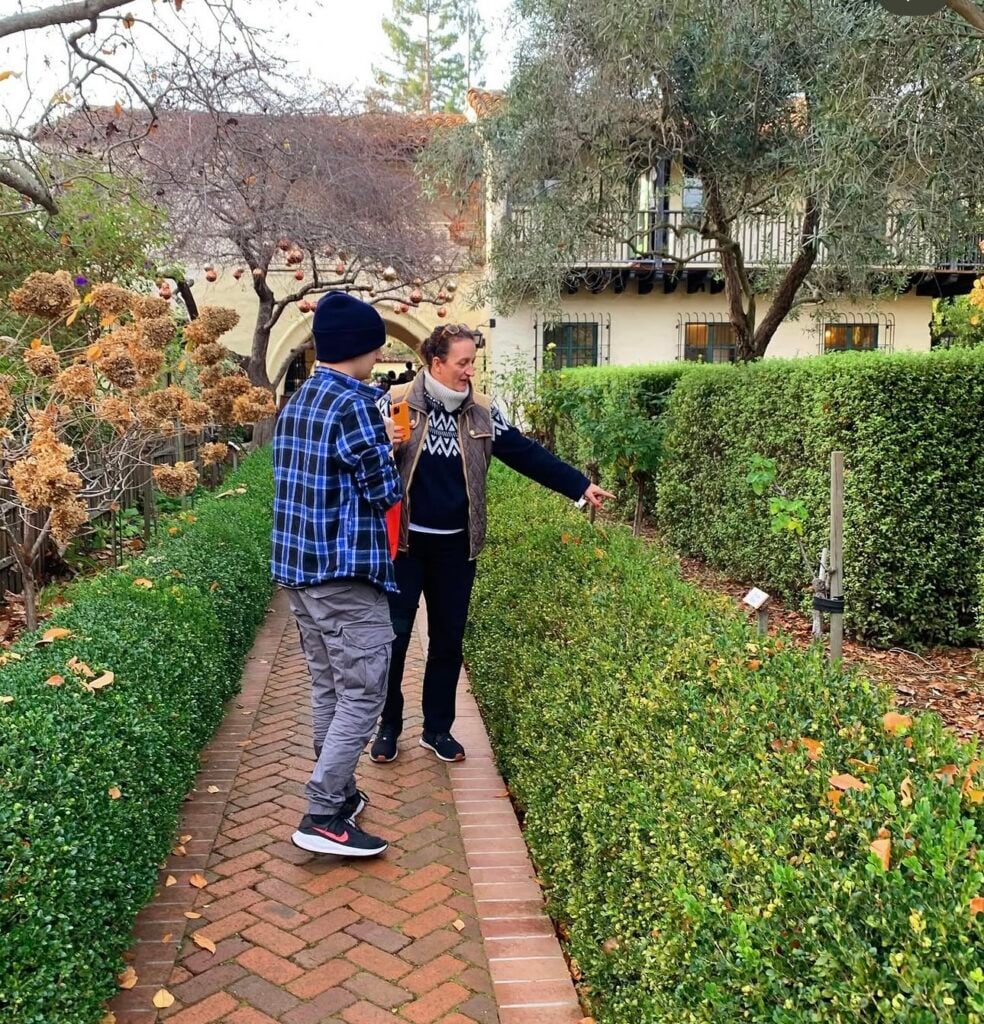 Two people walk down a brick path with hedges on either side admiring a plaque