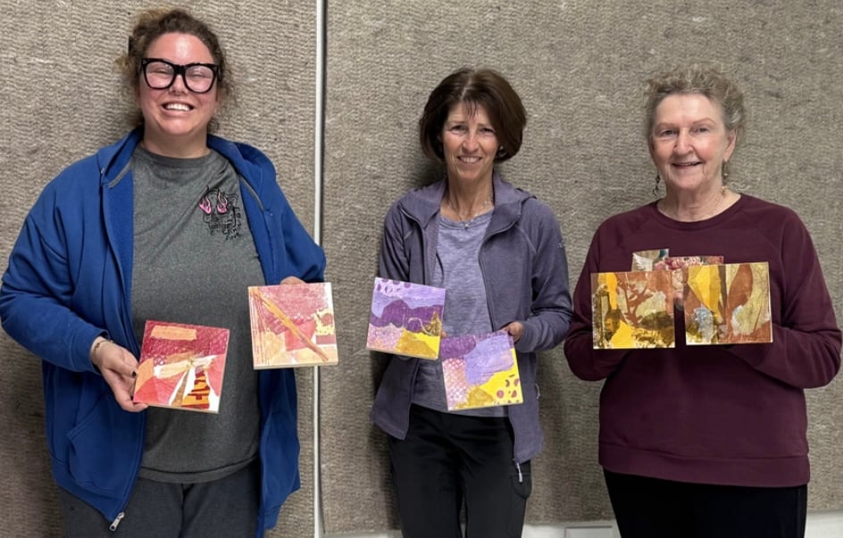 Three people hold up paintings they made in a Detati Art Class