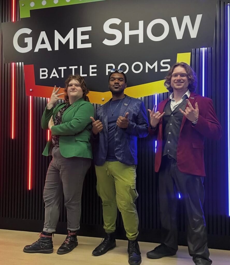 Team member pose in front of the Game Show Battlerooms sign while wearing colorful blazers