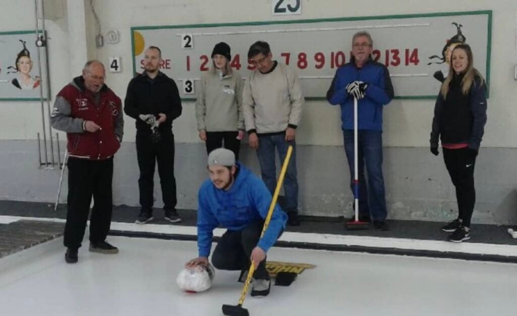 A curler squats on the rink at Granite Curling Club while team members look on
