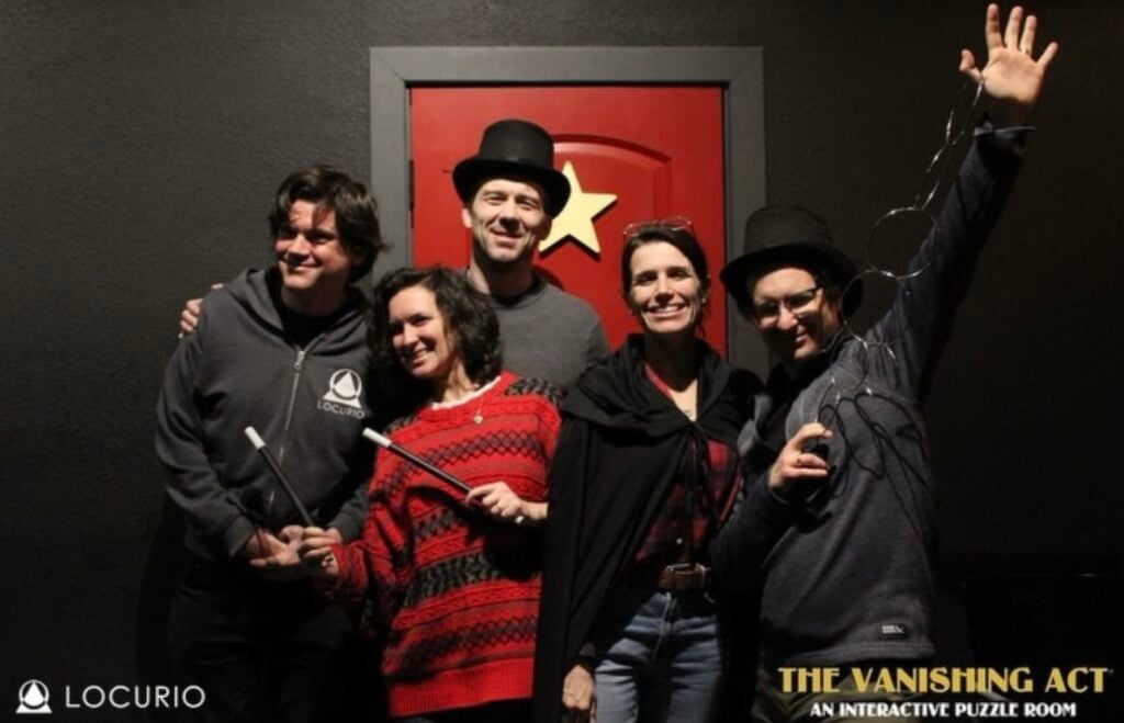 Team members pose in front of a door with a star bearing silly magician hats and wands