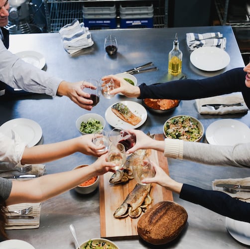 Team members cheers across the table at a Gourmandise School cooking class