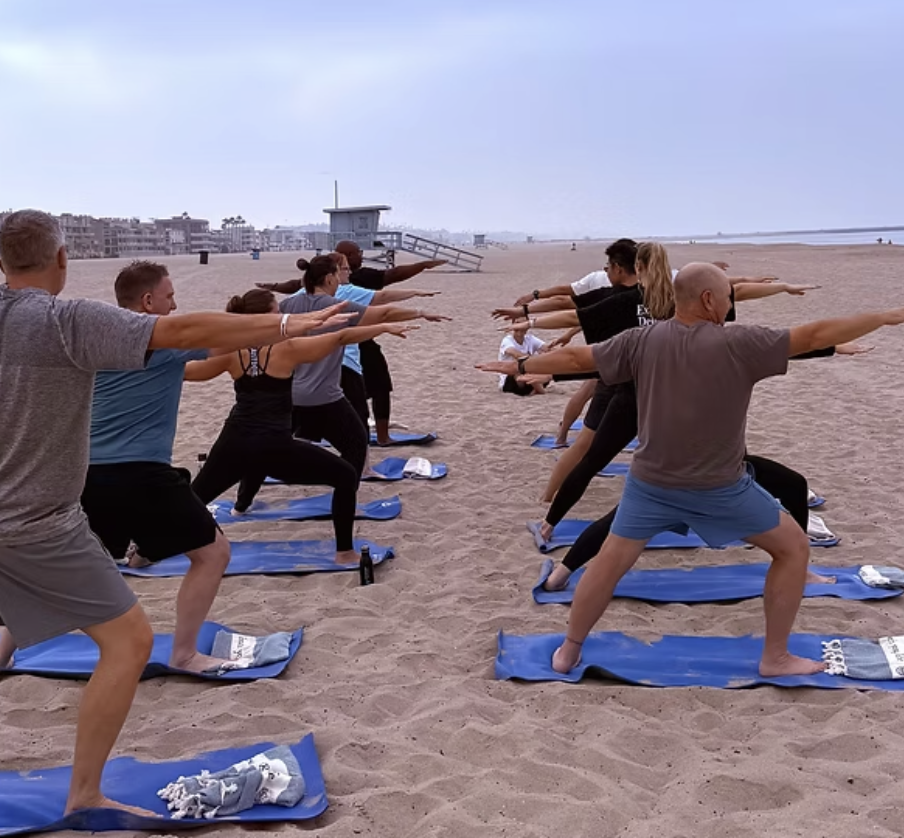 A team hits the warrior pose during a beach yoga class
