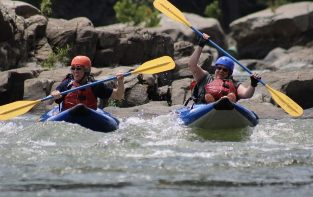 Two kayakers raise up their oars as they paddle