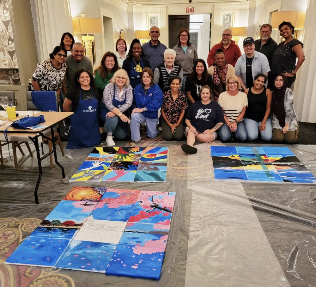 After a successful Sip and Paint a team poses next to their masterpieces