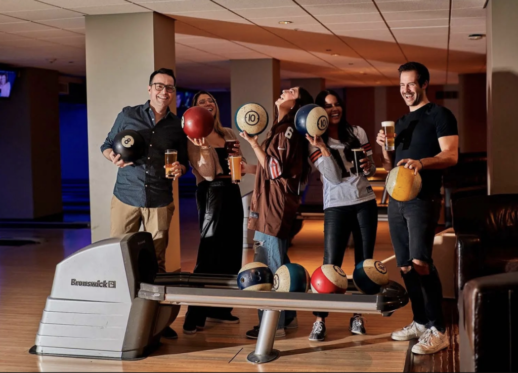Coworkers hold bowling balls aloft at Pinstripes during a team building event