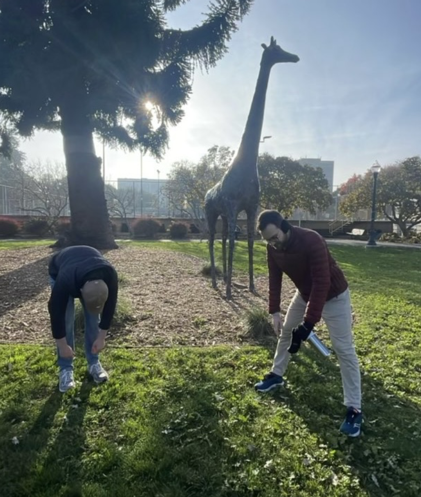 Team members pose in a silly configuration in front of a giraffe statue