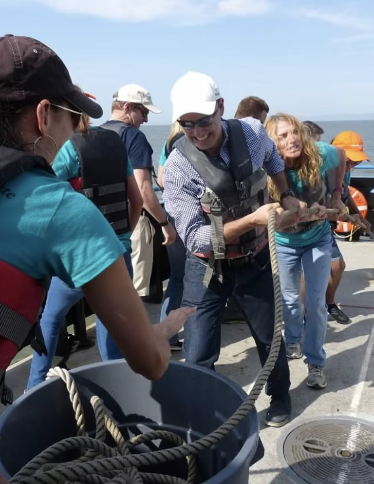 Team members hoist a rope on a boat on the SF Bay