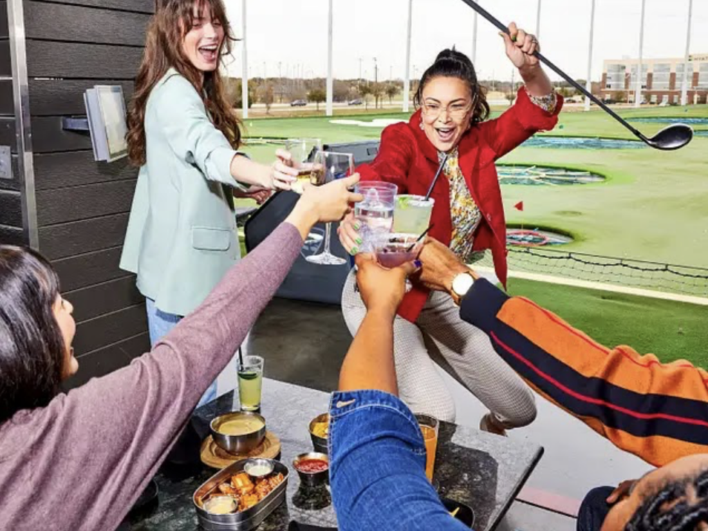 Coworkers cheers and raise their golf clubs high at Topgolf