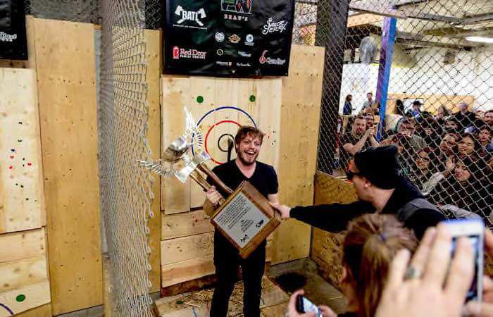 The best axe thrower of the day holds a trophy in front of the target