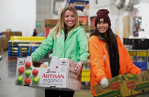 Coworkers beam while trransporting organic produce at a volunteering event for Food Lifeline