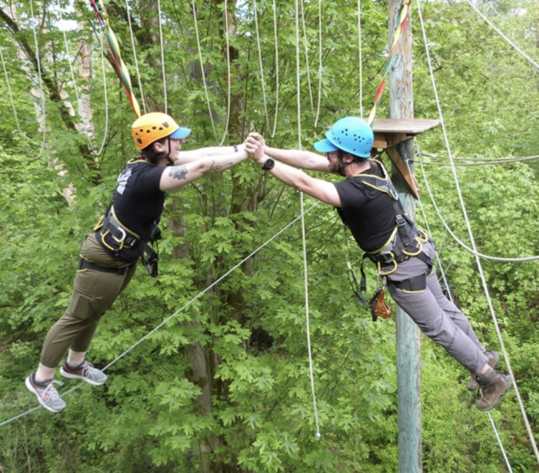 Team members hold hand in the sky as they hang from ropes over top of the trees