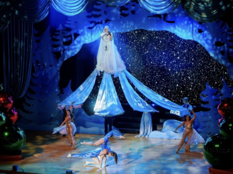 A woman in a pretty dress floats above the stage as blue lights and white snow fall around her
